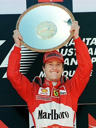 Eddie Irvine lifting a trophy on a Formula 1 podium.