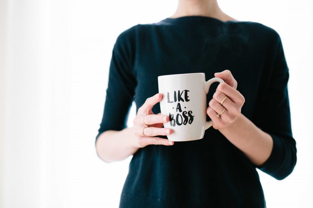 Shallow-focused woman shown from the neck down holding a coffee mug that says 'Like a boss' on it. 