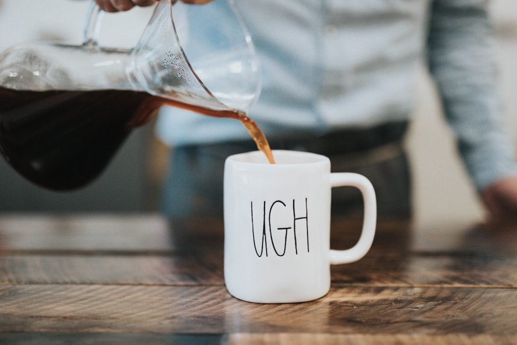 Coffee being poured into a cup with the word 'Ugh' written on it.
