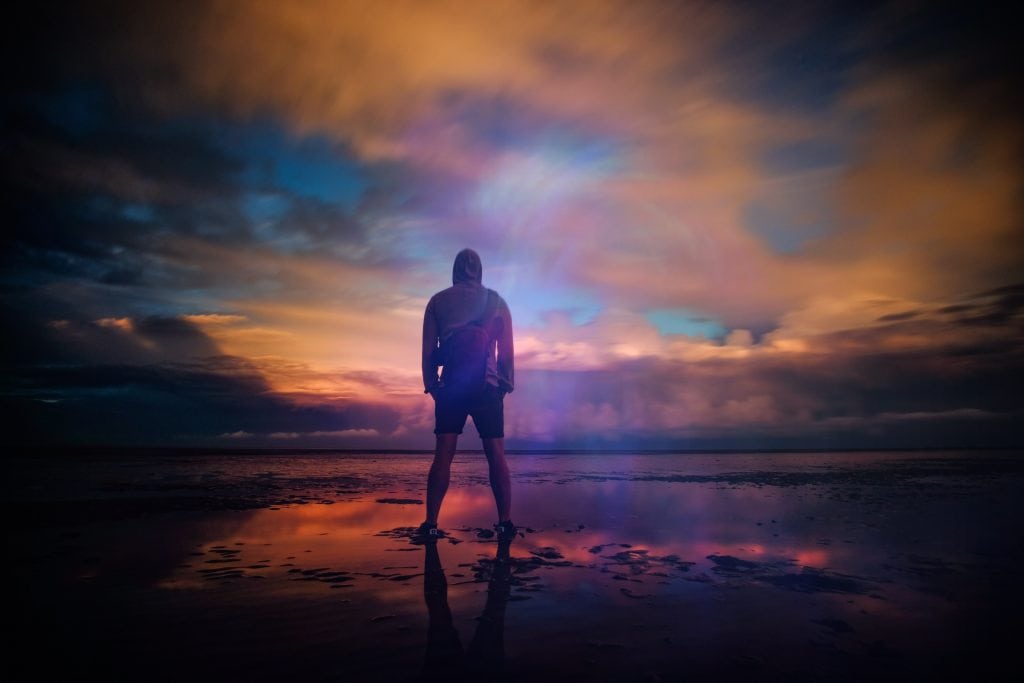 Dramatic shot of man standing on the shore at sunset.