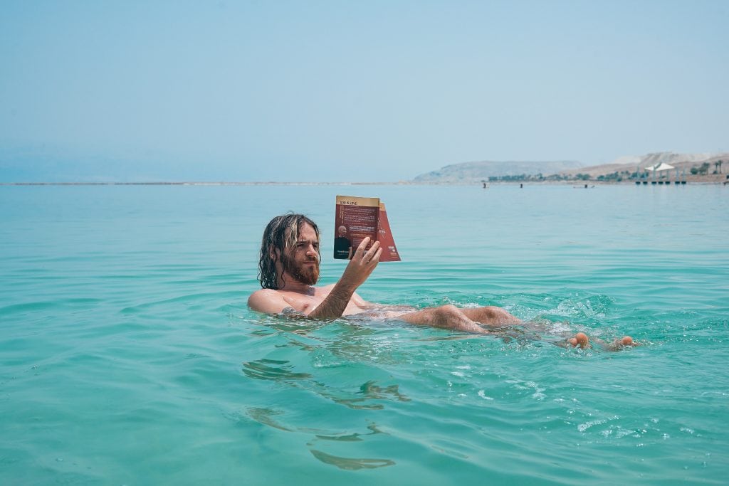 Long-haired man floating in the ocean while reading a book.