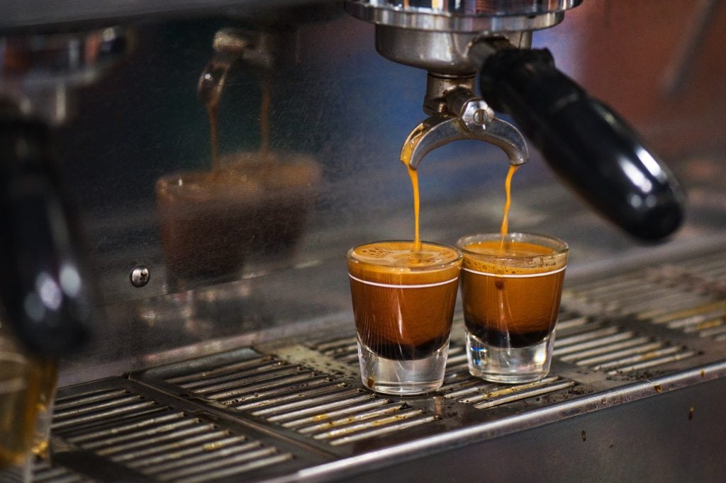 Two glass espresso cups being filled by the spouts of an espresso machine.