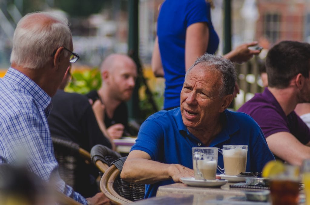 Two elderly men chatting at a table in a coffee shop.