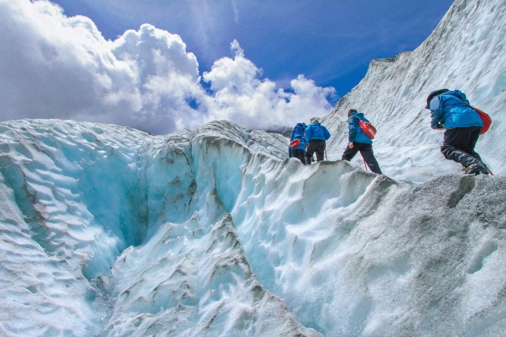 Four climbers walking up a steep mountainside covered in ice and snow.