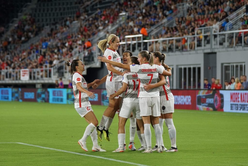 Group of six female soccer players celebrating a goal/