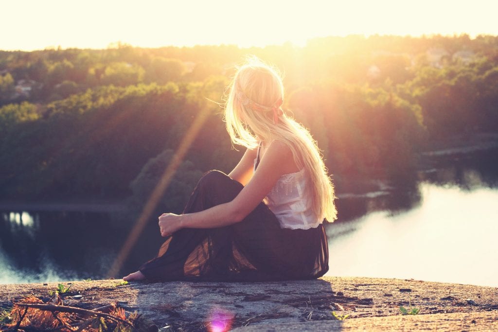 Young woman sitting on a hilltop overlooking a lake at sunset