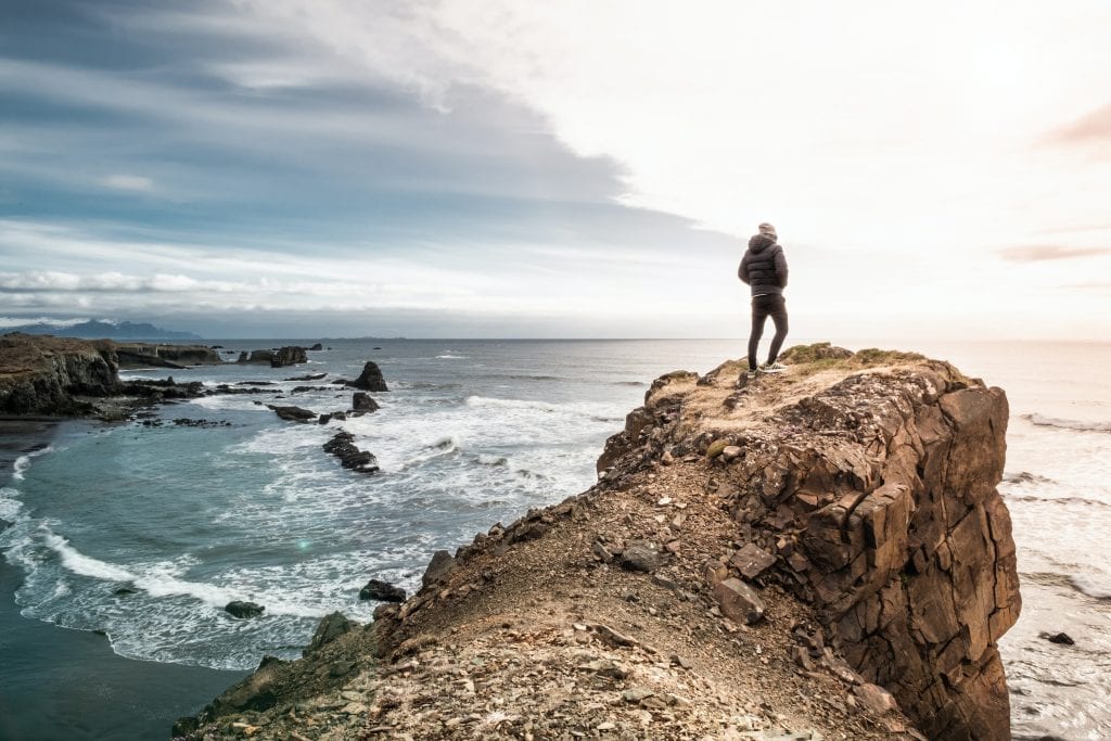 Man standing on the top of a cliff overlooking the sea
