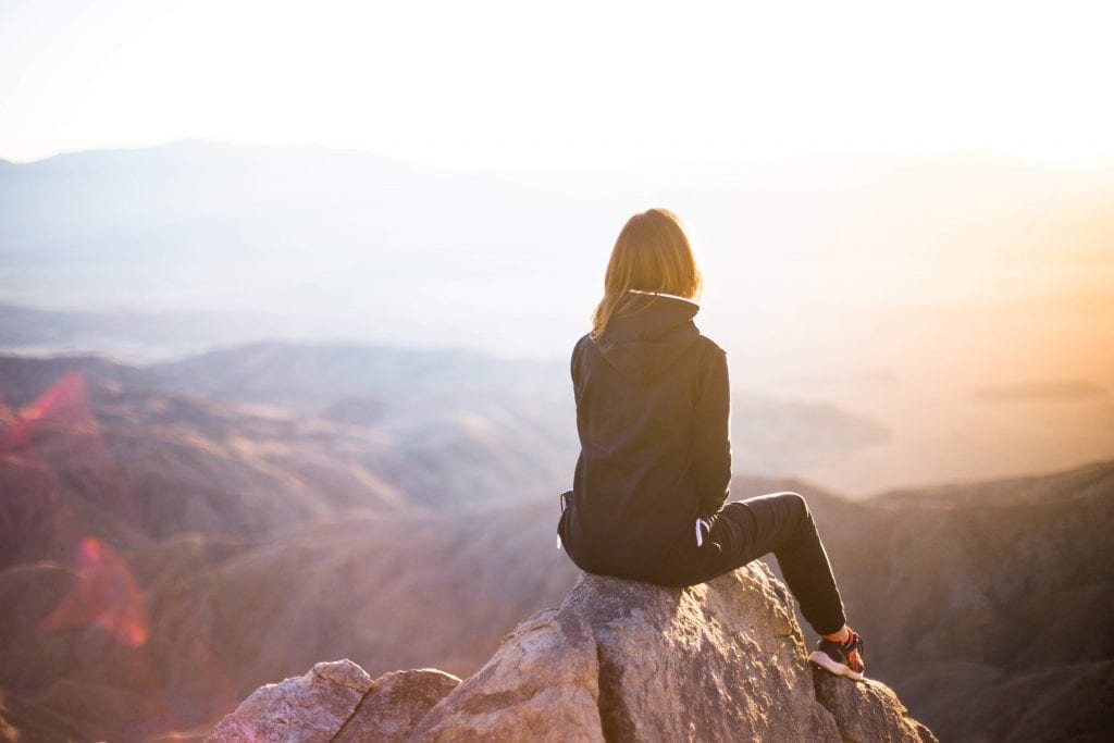 Woman sitting on a rock overlooking a mountain range at sunset.
