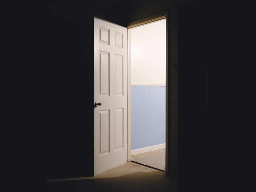 Door open from dark room with light coming through it on the other side.