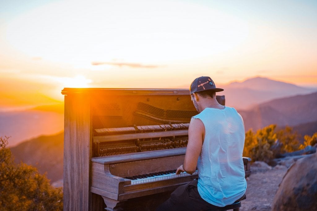 Man playing a piano overlooking a mountain range at sunset.