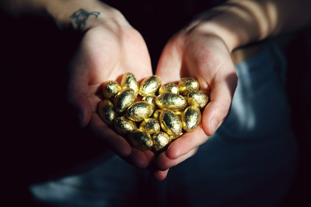 Close up of a pair of hands holding a bunch of golden eggs.