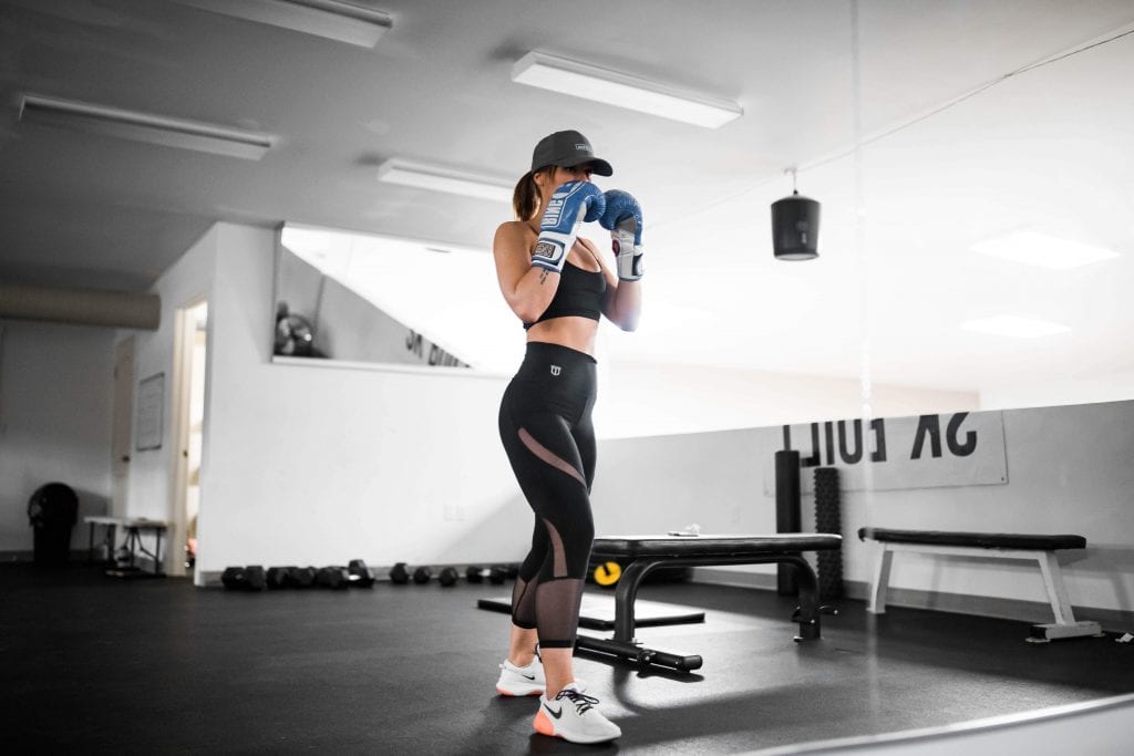 Woman in gym clothes and boxing gloves in gym.
