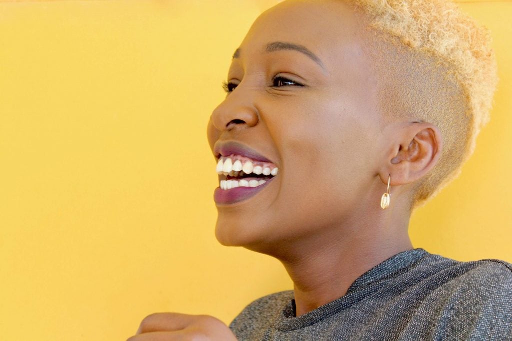 Young woman with yellow hair smiling against a bright yellow background.