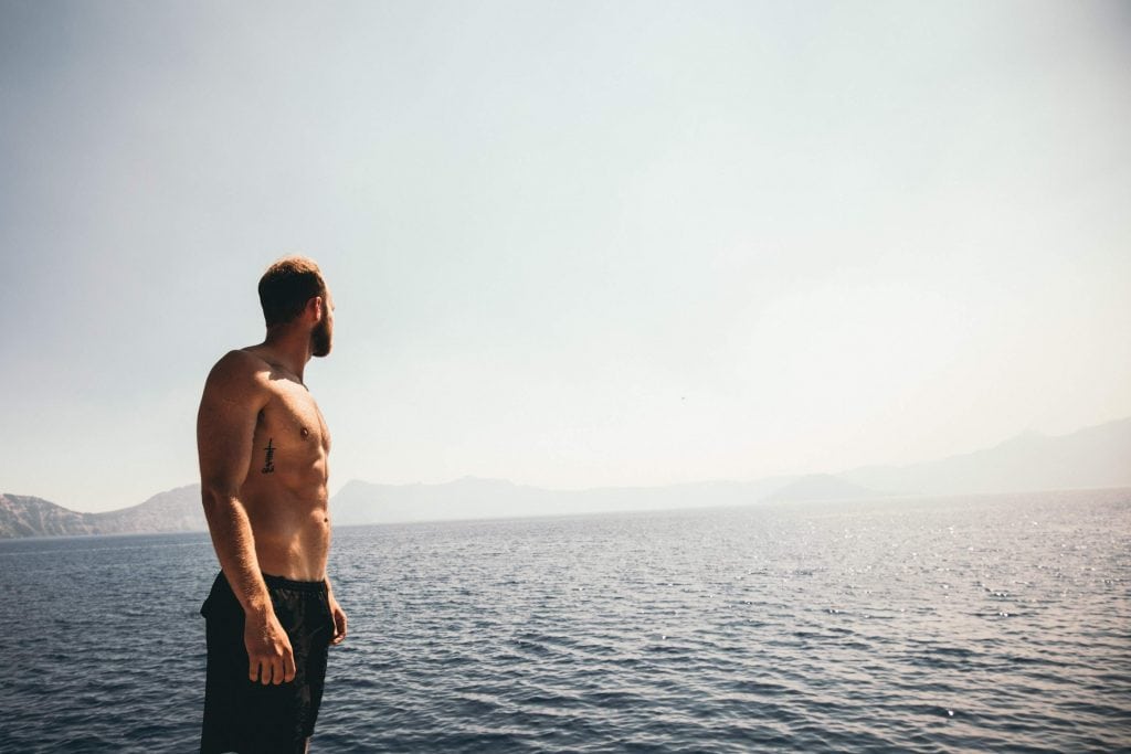 Shirtless man in black shorts standing at the edge of the sea.