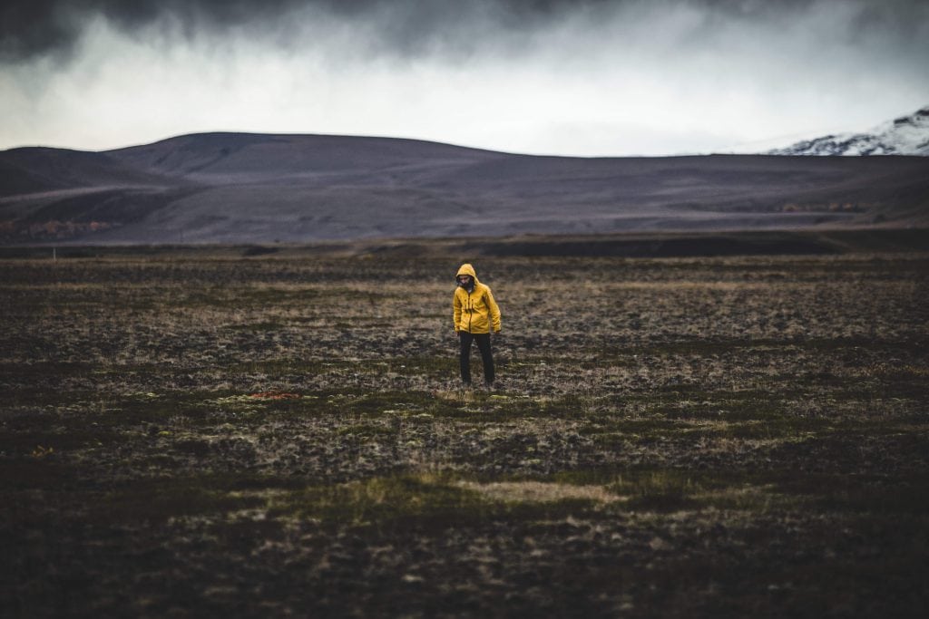 Man in yellow coat walking along vast landscape under stormy sky.