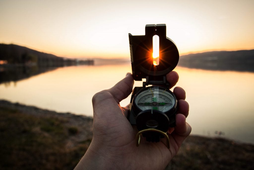 First-person point of view of a hand holding a compass against a setting sun.
