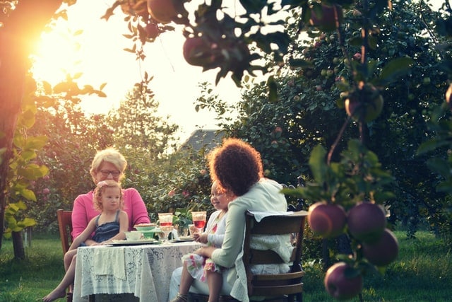 Two women with young children on their lap, enjoying a meal in their garden at sunset.