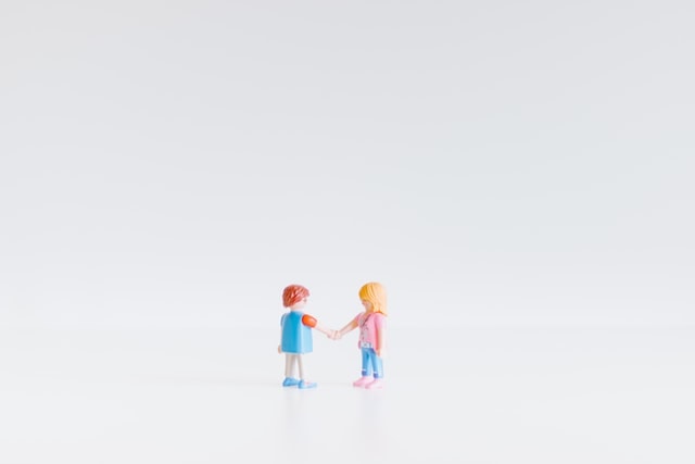 Plastic figurines of a boy and girl shaking hands against a blank background.