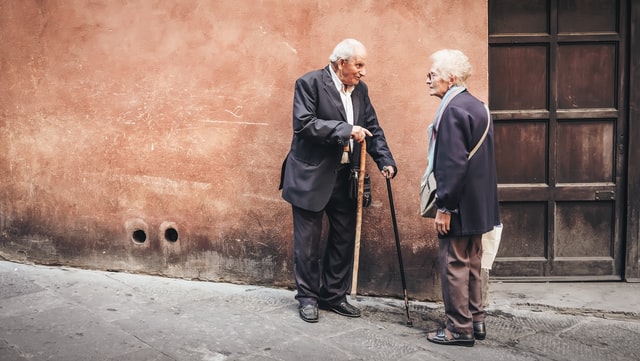 Old man with a cane talks to a woman in the street.