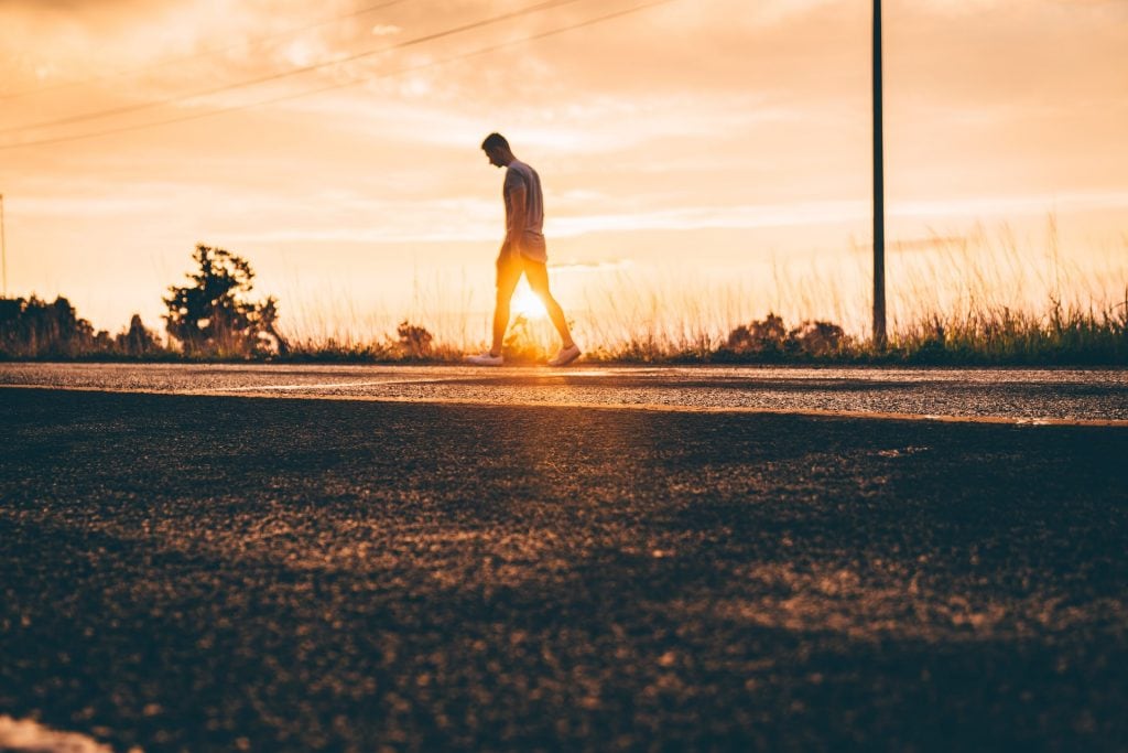 Man walking along a road at sunset.