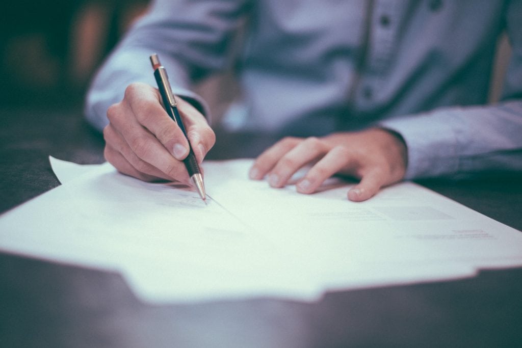 Shallow depth shot of man signing papers with pen.