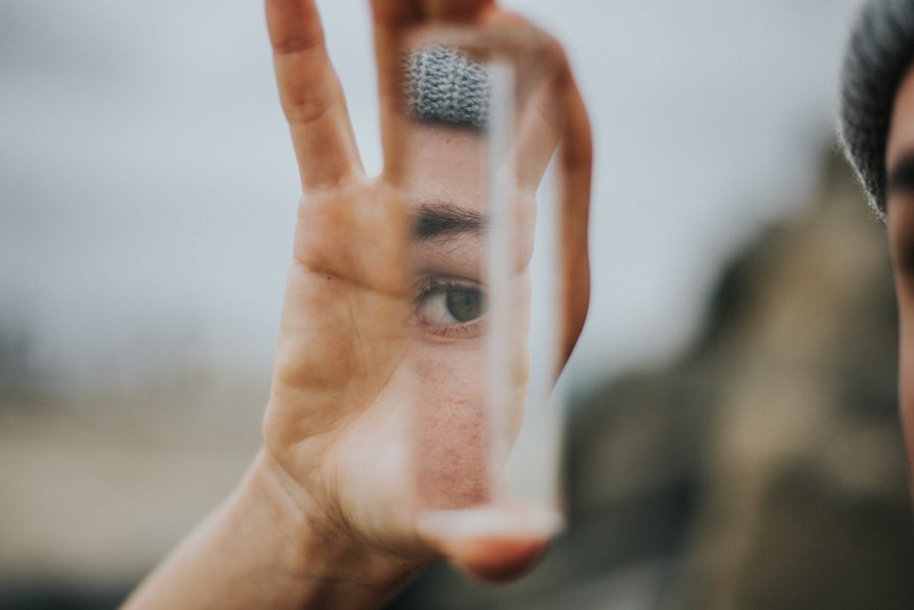 Shallow focus of person holding a narrow mirror between their fingers, with an eye reflecting in the mirror.