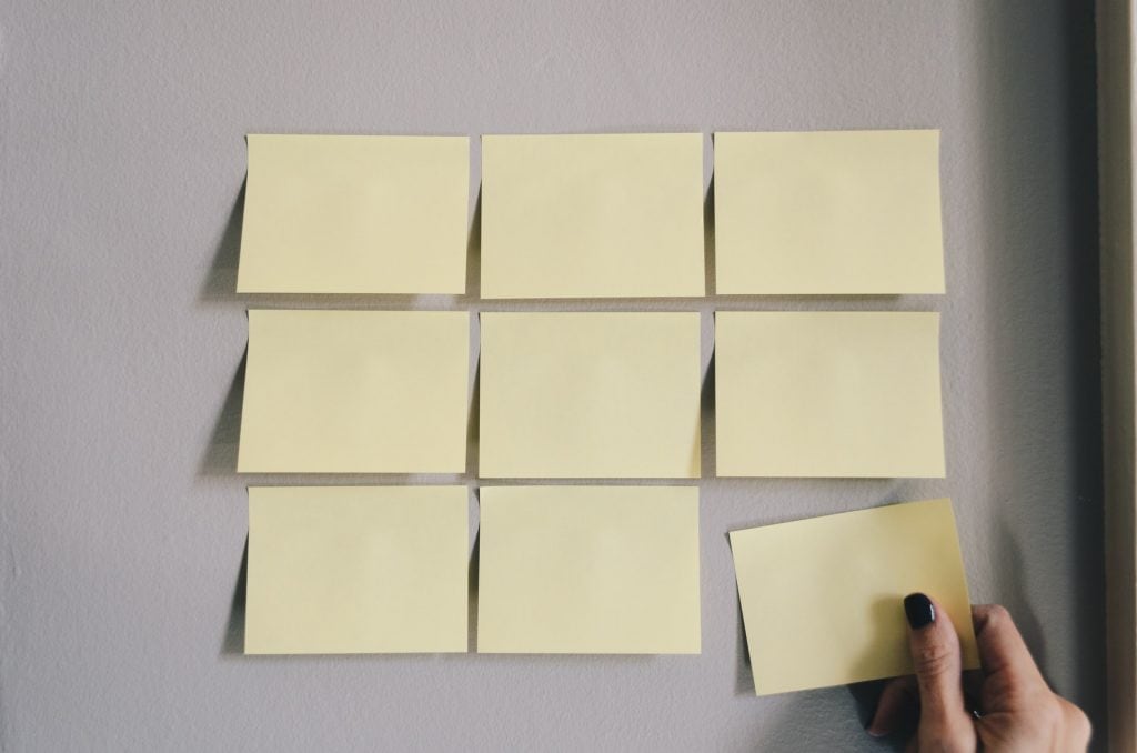 Nine yellow sticky notes in three neat rows on a wall.