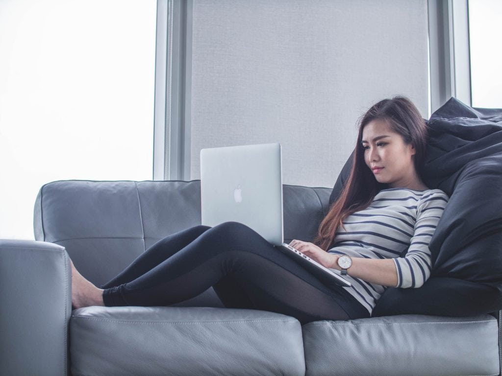 Woman working on a laptop on her couch at home.