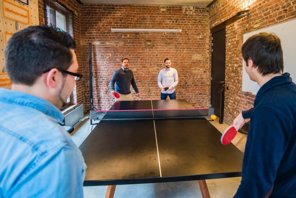 Four male workers playing table tennis in an office.