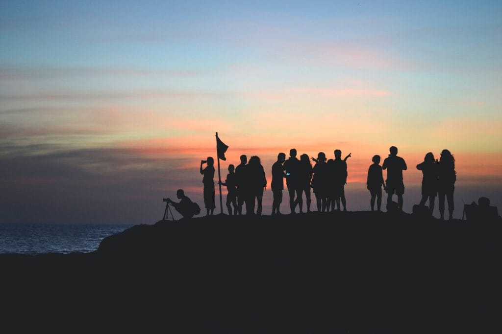Silhouette of several people standing on a low cliff overlooking the sea at sunset.
