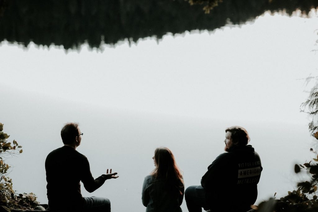 Two men and a woman talking on a riverbank.