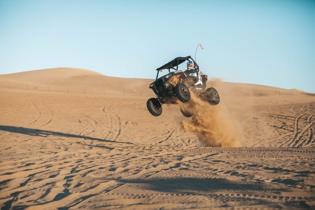 Person driving in a UTV in the desert and getting launched into the air over a dune.