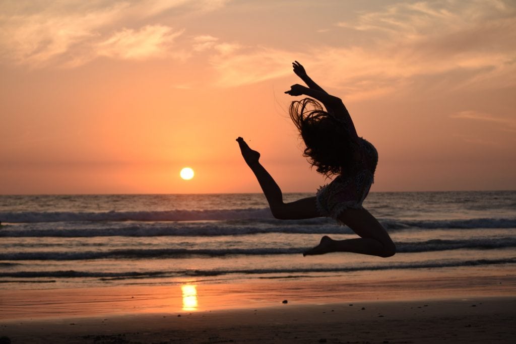 Silhouette of a woman jumping on the beach at sunset.