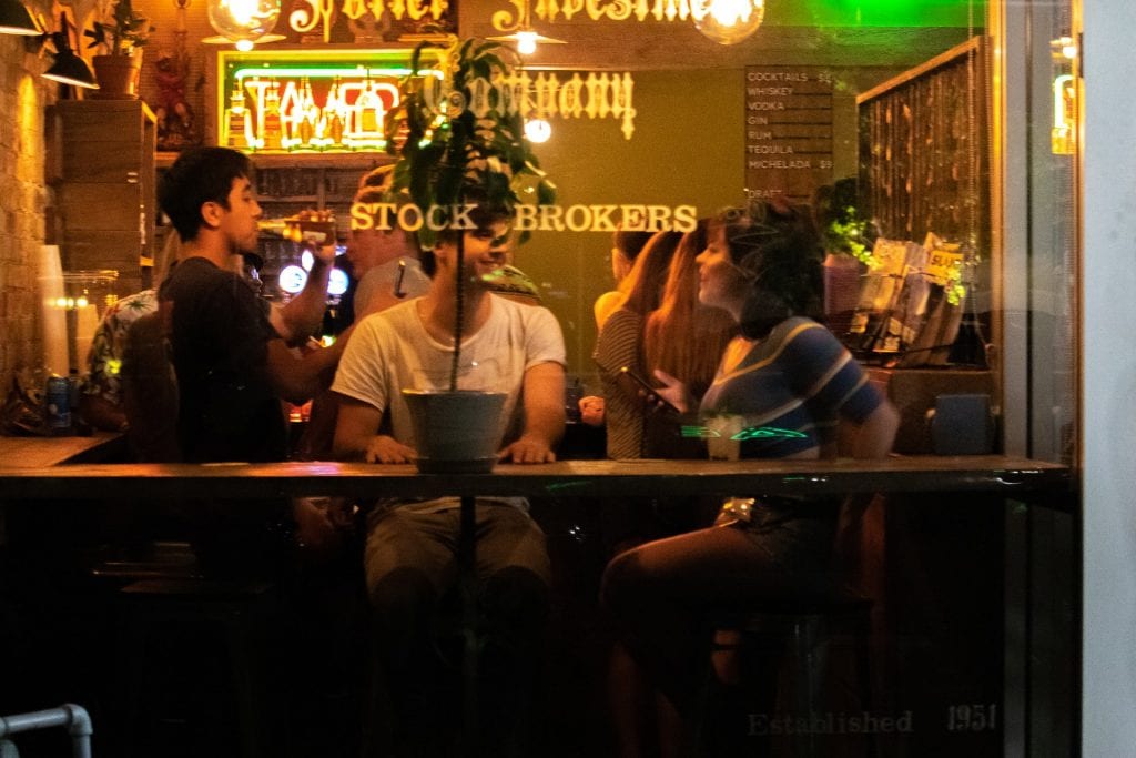 Three people seen enjoying themselves behind a bar window at night.