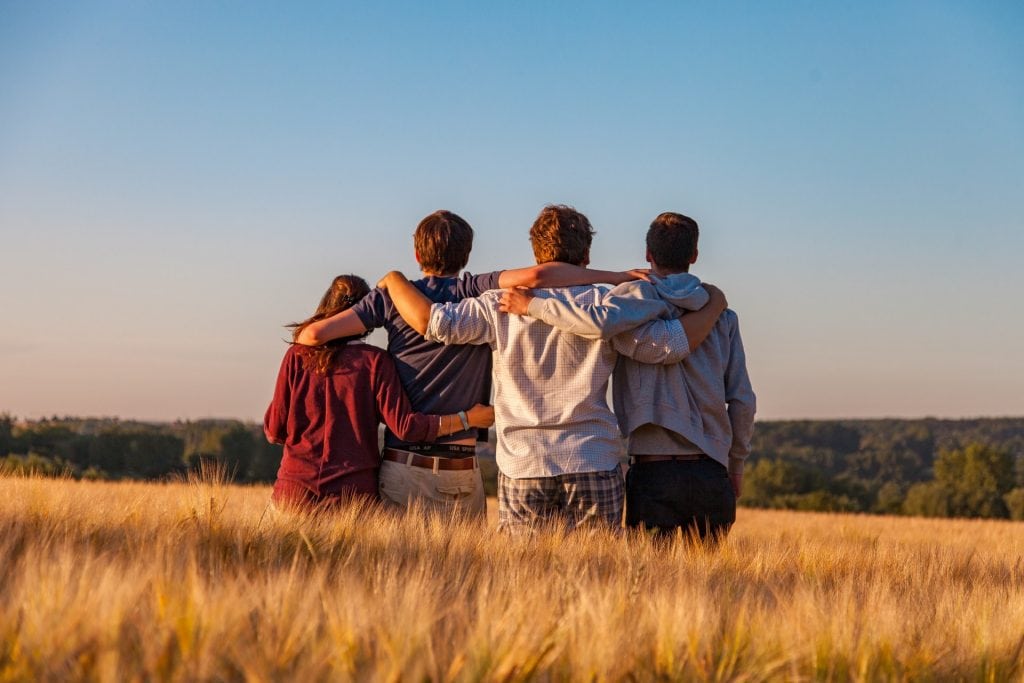 Backview of four people standing in a field, arm-in-arm.