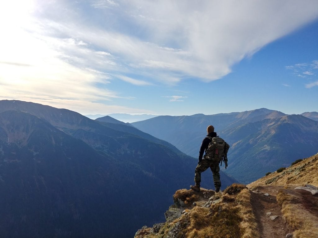 Back view of a man standing on top of a mountain overlooking a vast mountain range.