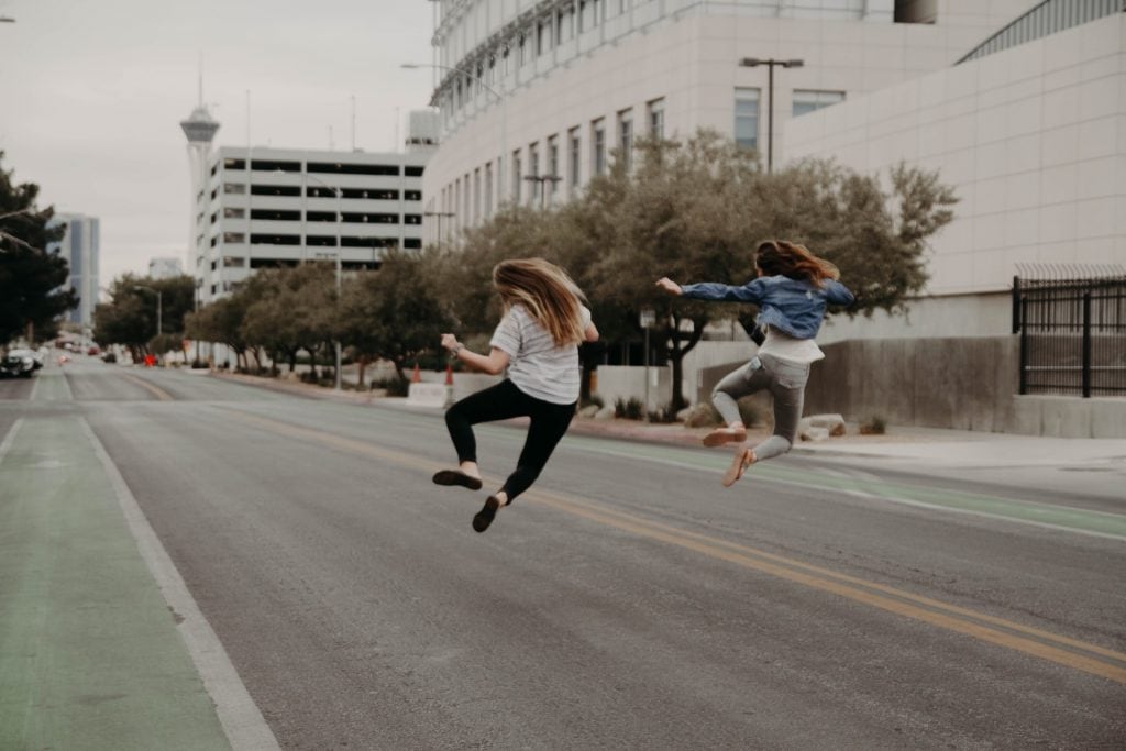 Two woman jumping and clicking their heels together in the street.