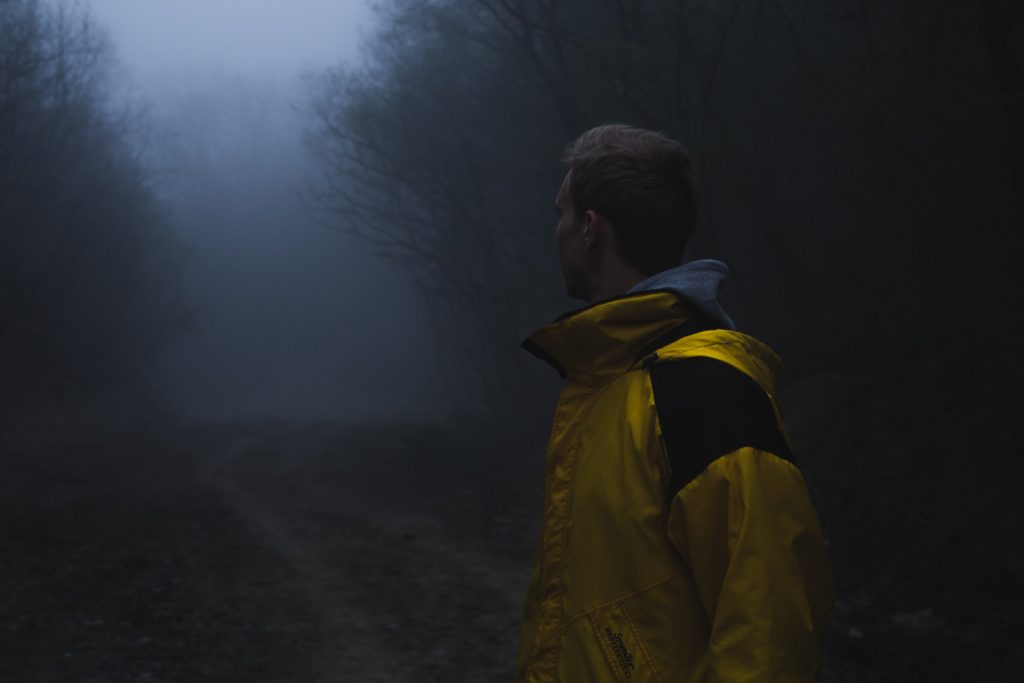 man in yellow jacket standing in misty, haunted looking woods