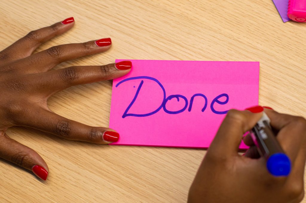 close up of woman's writing the word 'done' on a pink post-it note
