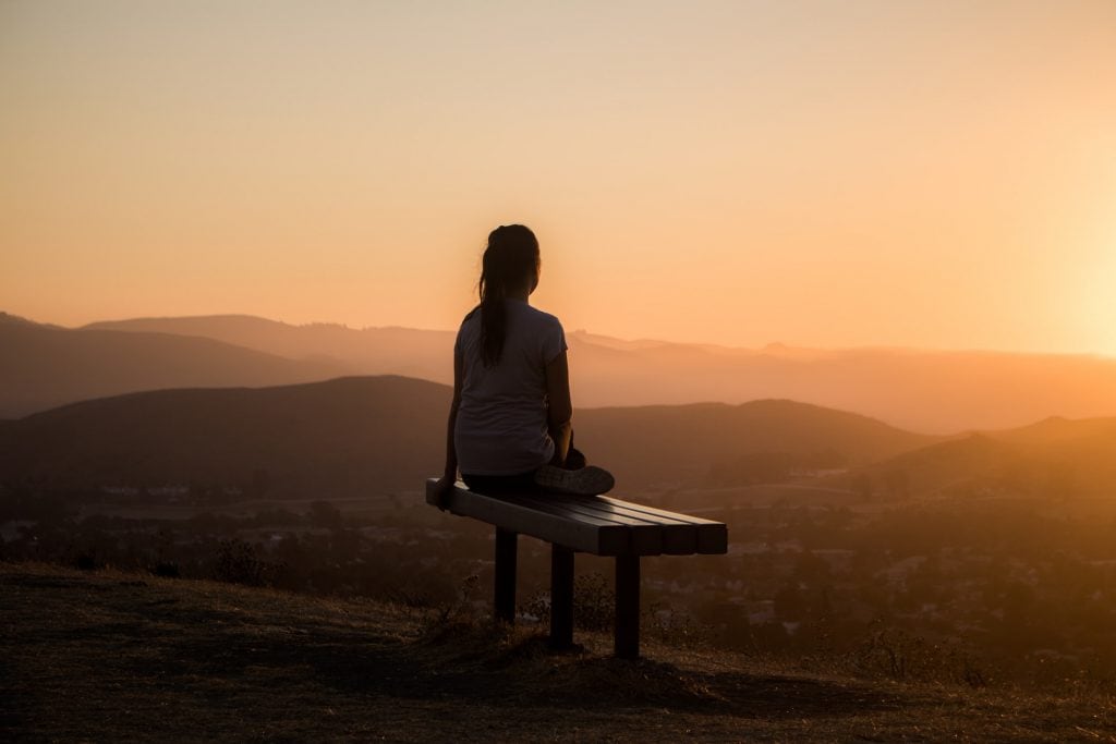 silhouette of woman sitting on a bench overlooking mountains at sunset
