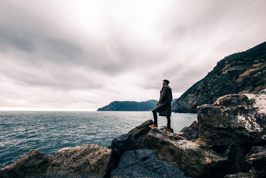 man standing on a boulder, looking out at the ocean