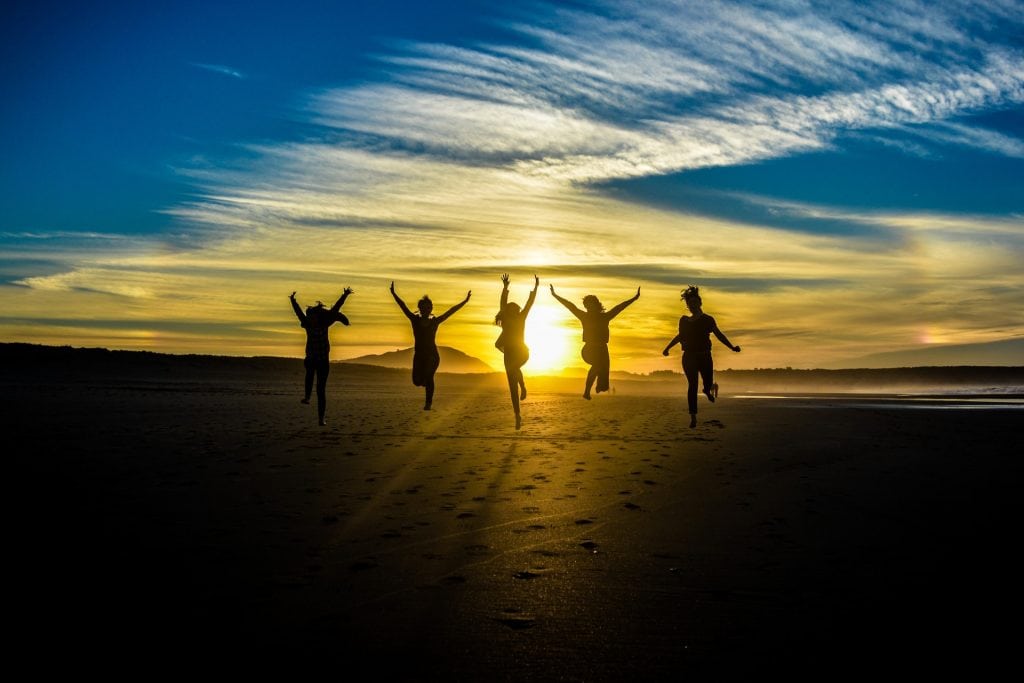 silhouette of five people jumping on a beach at sunset